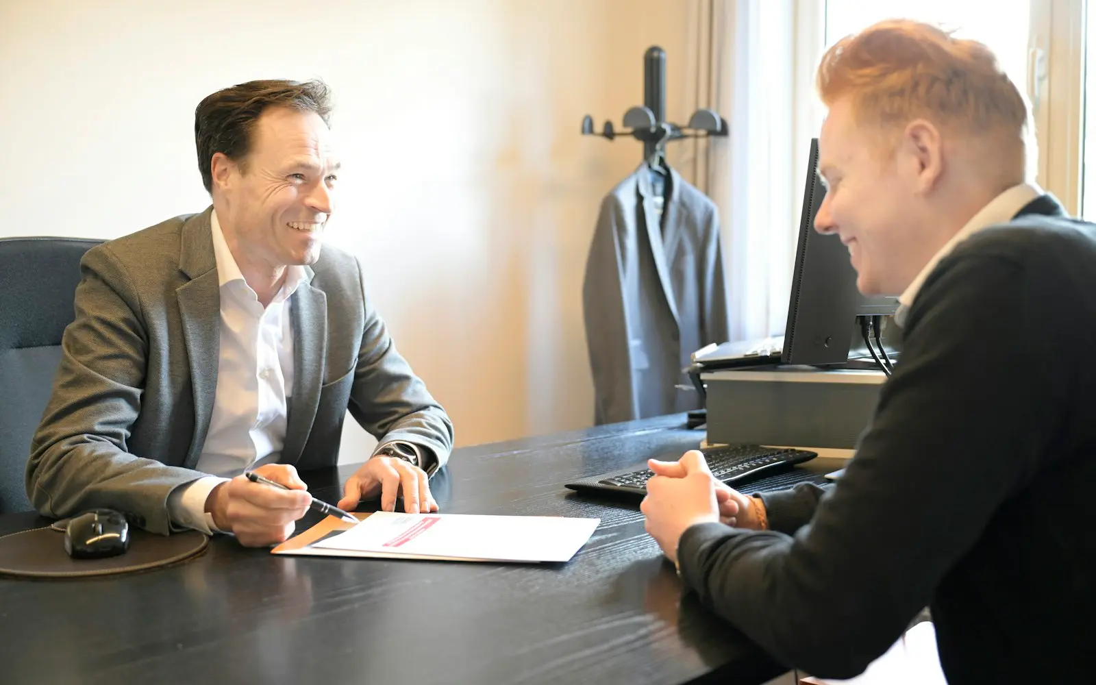 Two men discussing documents across an office desk